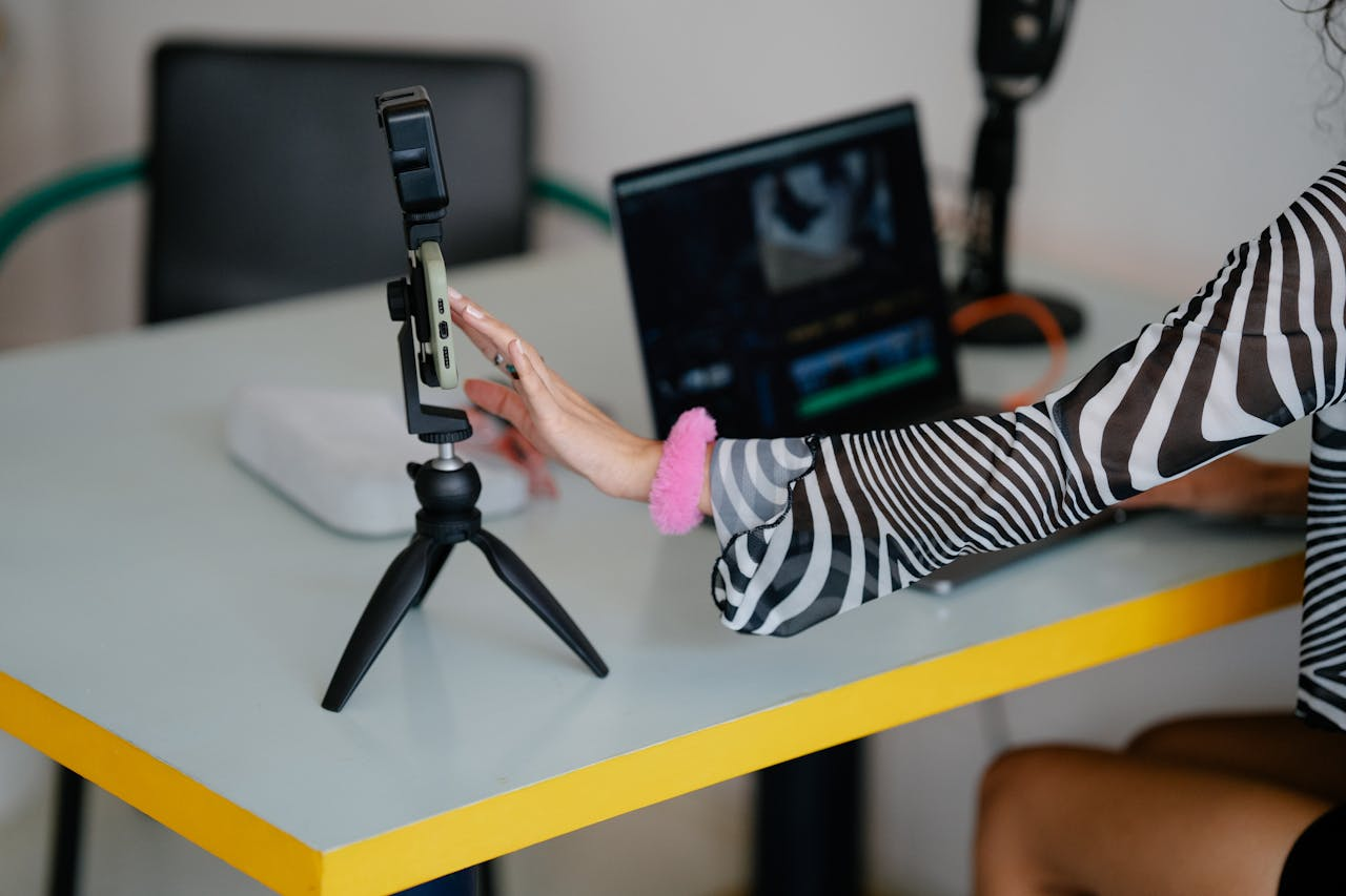 Home Woman adjusting smartphone on tripod with laptop setup for video editing.