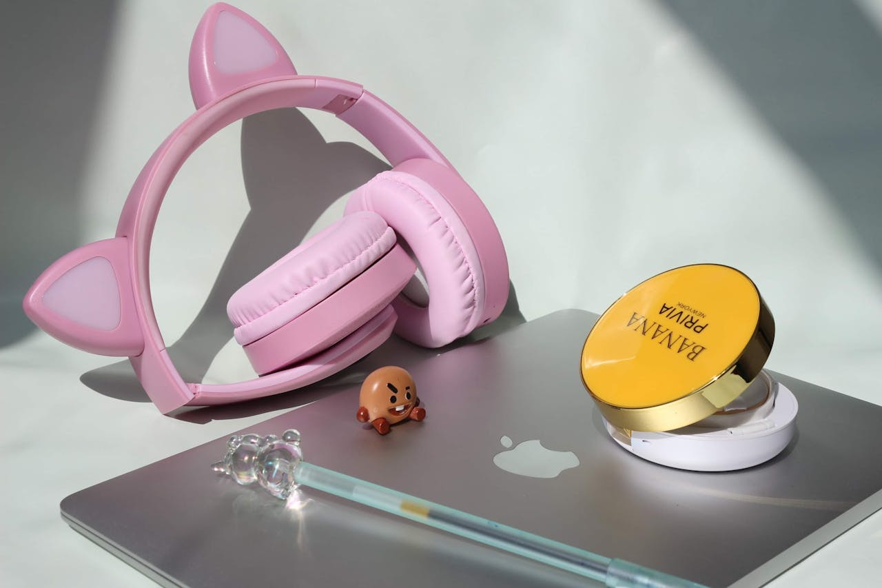 expertise-01 Stylish pink cat ear headphones resting on a sleek laptop with cosmetics.